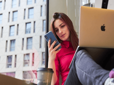 A picture of a girl using her phone with a laptop on her lap.